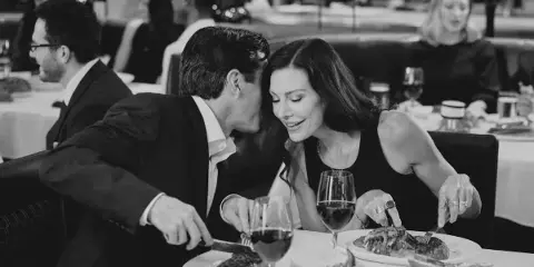A couple enjoying a steak dinner in an upscale restaurant with wine glasses and other diners in the background.