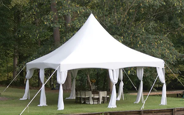 White event tent with draped fabric set up on a grassy lawn with tables and chairs underneath.