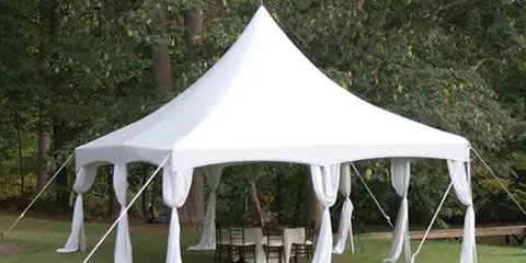 White event tent with draped fabric set up on a grassy lawn with tables and chairs underneath.