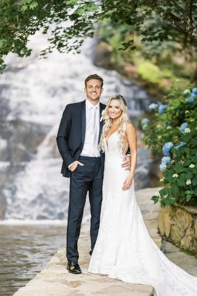 A bride and groom standing together in front of a cascading waterfall at a wedding venue.