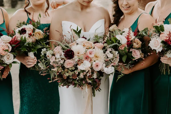 A bride in a white gown and bridesmaids in green dresses holding floral bouquets.