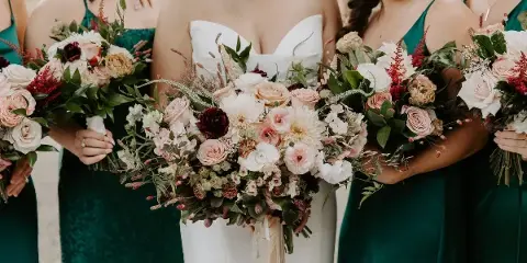 A bride in a white gown and bridesmaids in green dresses holding floral bouquets.