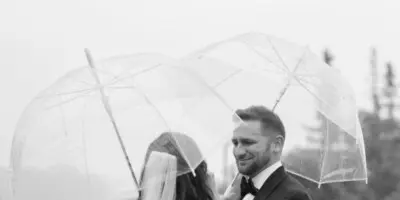 A bride and groom embrace under clear umbrellas during a rainy outdoor wedding first look.