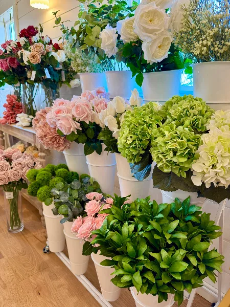 A display of various real-touch floral stems, including roses and hydrangeas, arranged in white buckets inside a floral studio.
