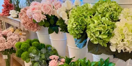 A display of various real-touch floral stems, including roses and hydrangeas, arranged in white buckets inside a floral studio.