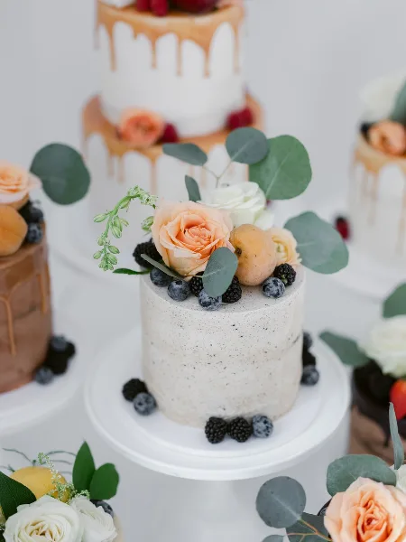 A display of custom cakes decorated with fresh flowers and berries.