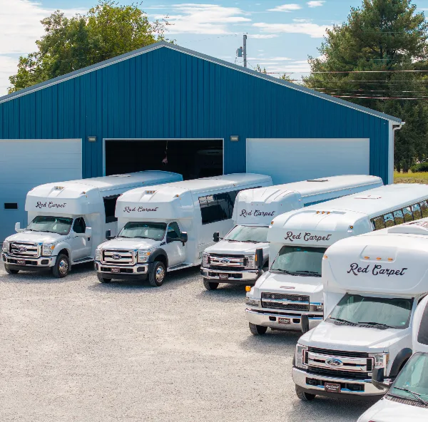 A fleet of white Red Carpet party buses and shuttles parked in front of a blue garage.