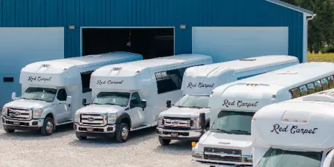 A fleet of white Red Carpet party buses and shuttles parked in front of a blue garage.