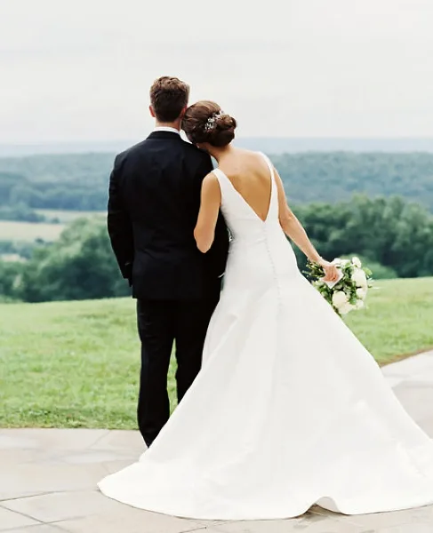 A bride and groom standing together on a stone patio overlooking a green landscape.