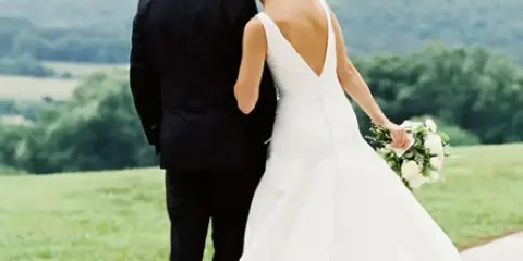 A bride and groom standing together on a stone patio overlooking a green landscape.