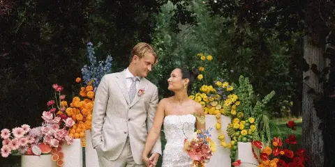 A bride and groom holding hands in front of colorful floral pedestals and greenery.