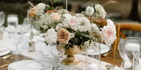 Styled wooden event table set with white plates, glassware, candles, and a floral centerpiece