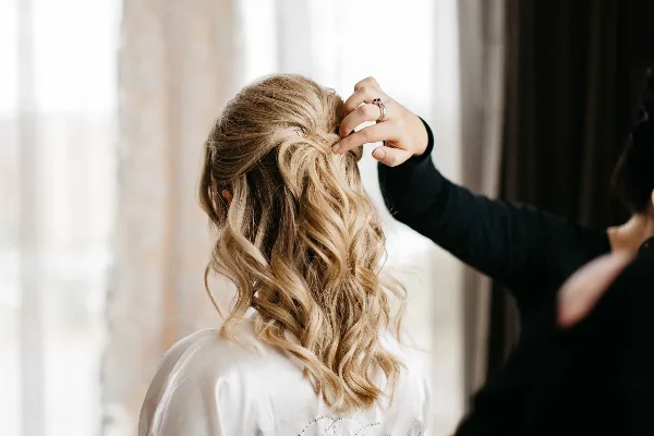 A professional stylist styling a bride's blonde hair into an elegant updo.