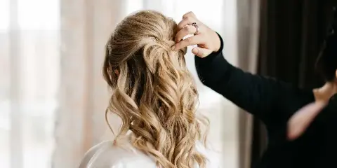 A professional stylist styling a bride's blonde hair into an elegant updo.