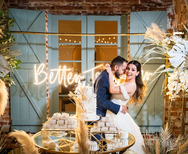 A bride and groom embracing at a wedding reception with a decorated cake and floral arrangements.