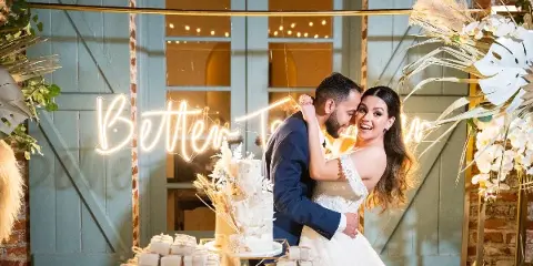 A bride and groom embracing at a wedding reception with a decorated cake and floral arrangements.