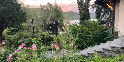 A view of the Brookwood Point lakeside garden venue featuring stone steps, string lights, and a view of the lake and mountains at sunset.