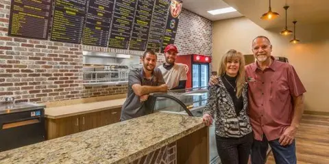 The Paisan's family at the deli counter, in front of the menu wall