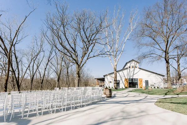 Outdoor wedding ceremony setup with white chairs arranged in front of a white barn venue.