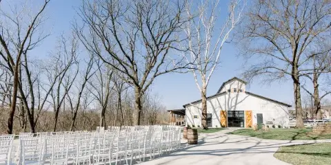 Outdoor wedding ceremony setup with white chairs arranged in front of a white barn venue.