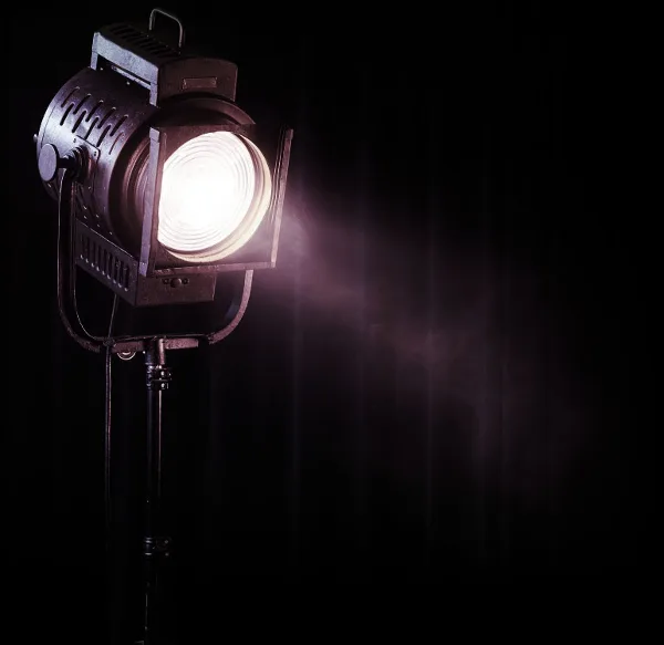 A professional stage spotlight on a stand, illuminated against a dark background.