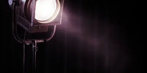 A professional stage spotlight on a stand, illuminated against a dark background.