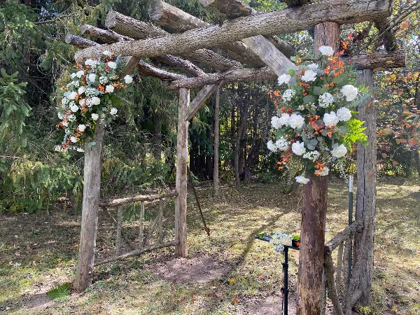 A rustic wooden wedding arch decorated with white and orange floral arrangements in an outdoor setting.
