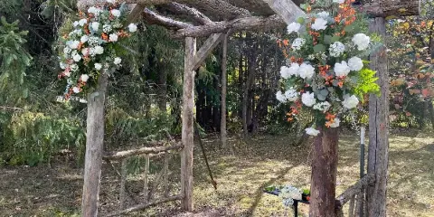 A rustic wooden wedding arch decorated with white and orange floral arrangements in an outdoor setting.
