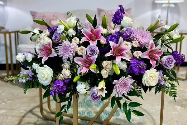 A large, elaborate floral arrangement with pink lilies, purple roses, and white flowers displayed on a gold stand.