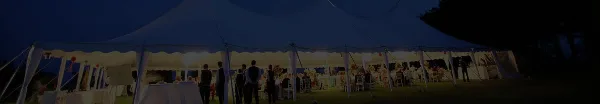 A large white event tent illuminated at night with tables and guests inside.