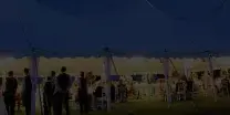 A large white event tent illuminated at night with tables and guests inside.