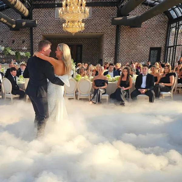 A bride and groom dancing on a fog-covered dance floor at a wedding reception with seated guests in the background.