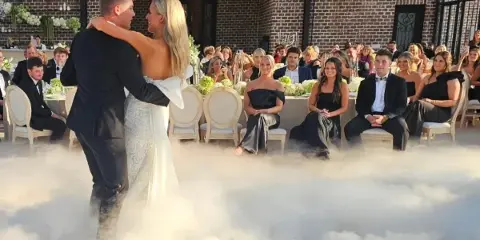 A bride and groom dancing on a fog-covered dance floor at a wedding reception with seated guests in the background.