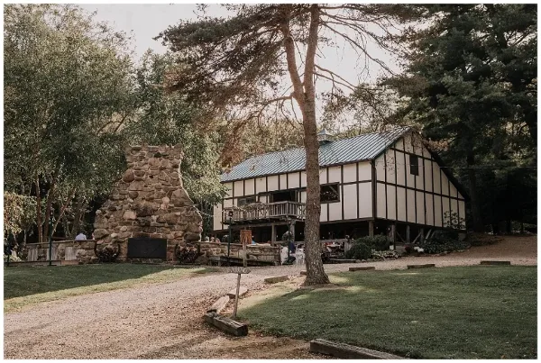 Exterior view of a timber-framed wedding venue building with a large stone fireplace in a wooded setting.