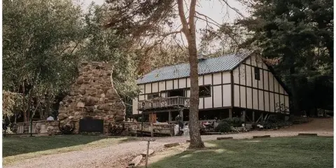 Exterior view of a timber-framed wedding venue building with a large stone fireplace in a wooded setting.