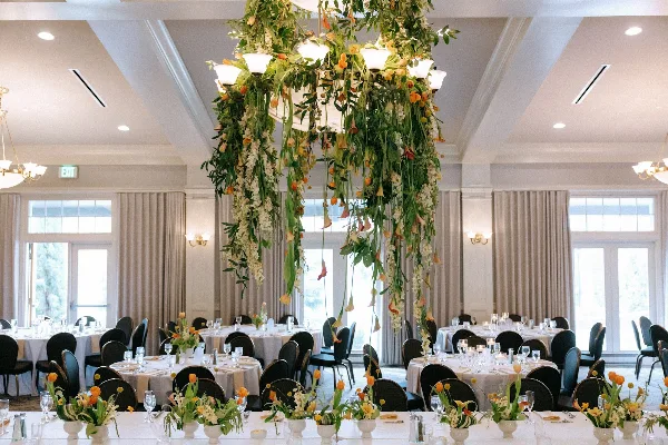 A wedding reception room featuring a large hanging floral chandelier installation and matching table centerpieces.