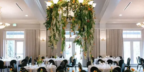 A wedding reception room featuring a large hanging floral chandelier installation and matching table centerpieces.