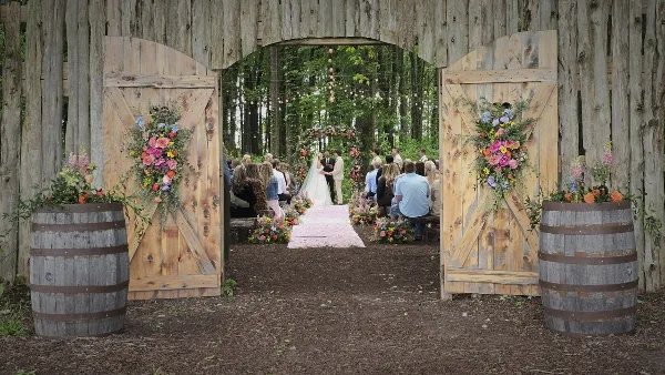 Outdoor wedding ceremony in a forest with rustic wooden barn doors and floral arrangements