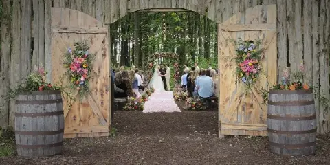Outdoor wedding ceremony in a forest with rustic wooden barn doors and floral arrangements
