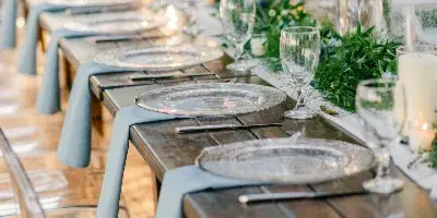 An outdoor wedding reception table set with silver charger plates, glassware, and a green floral runner.