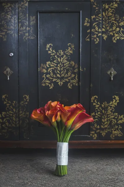 A bouquet of red and yellow calla lilies standing in front of a dark, gold-leafed cabinet.