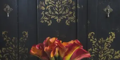 A bouquet of red and yellow calla lilies standing in front of a dark, gold-leafed cabinet.