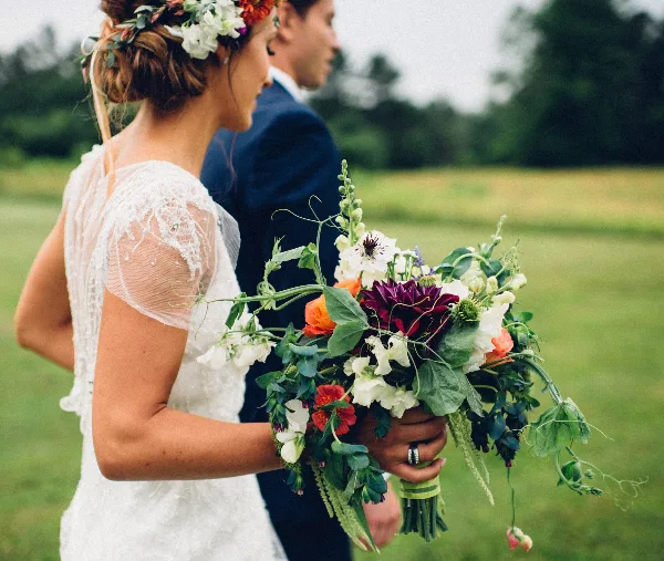 A bride holding a lush, seasonal wedding bouquet with mixed flowers and greenery.