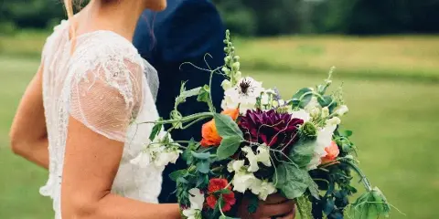 A bride holding a lush, seasonal wedding bouquet with mixed flowers and greenery.