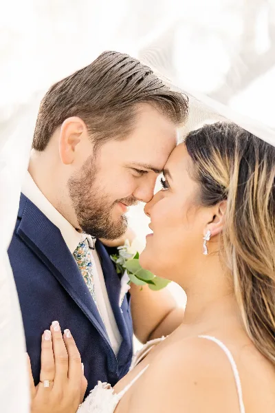 A close-up portrait of a bride and groom touching foreheads, with the bride wearing a veil and the groom in a navy suit.