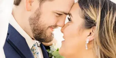 A close-up portrait of a bride and groom touching foreheads, with the bride wearing a veil and the groom in a navy suit.