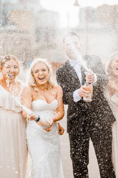 Bride and groom popping champagne bottles with guests at a wedding celebration