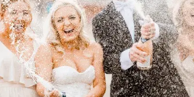 Bride and groom popping champagne bottles with guests at a wedding celebration