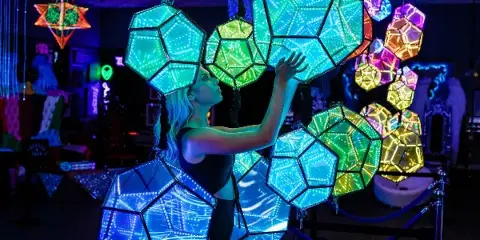 A person interacting with large, illuminated geometric LED art installations inside the OptiView 360 immersive studio.