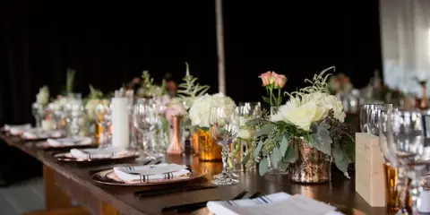 A long wooden table set for a wedding reception featuring white floral arrangements, candles, and copper accents.